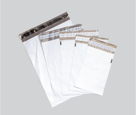 Un ensemble de cinq enveloppes plastiques blanches avec bandes adhésives de fermeture, disposées en éventail sur un fond gris clair. Les enveloppes sont de tailles variées et possèdent une bande métallique ou transparente sur le haut pour une fermeture sécurisée.