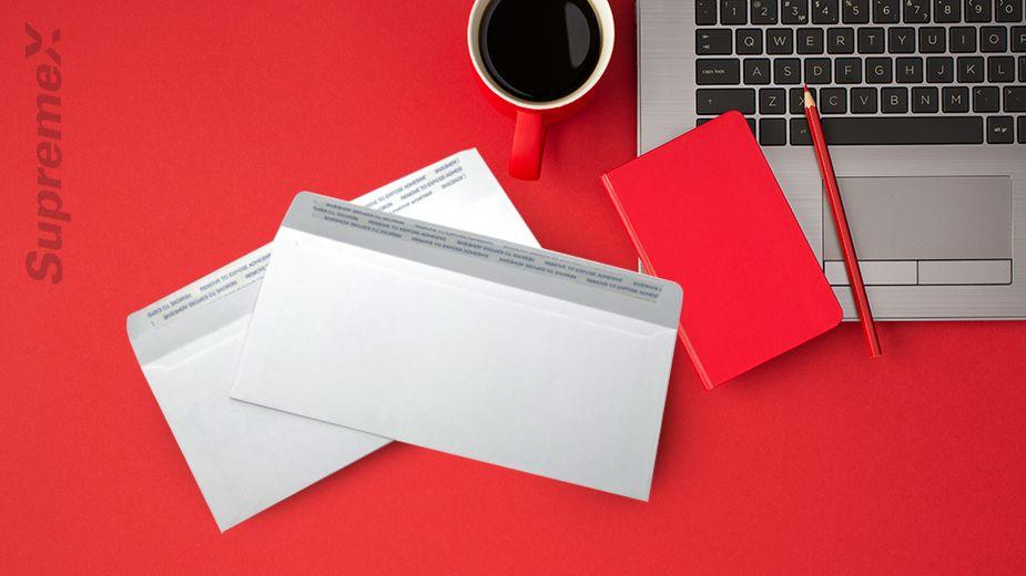 Une vue du haut d'une table avec un mug, un laptop, un crayon et un carnet et des enveloppe blanchs.