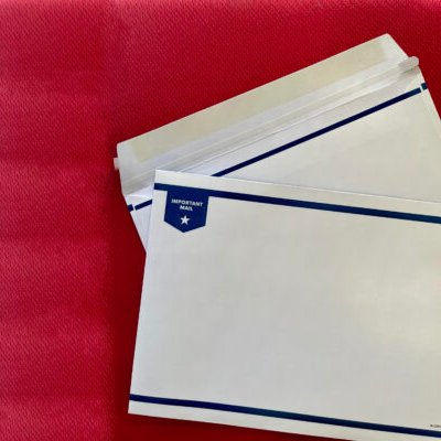 Deux Enveloppes en carton insérables mécaniquement en blanc dont une est ouverte avec une vue du verso. Contenant de la colle pour sceller et une ficelle à déchirure pour l'ouverture. Le côté recto contien deux lignes décoratives en bleu et un tag contenant la mention important et une étoile.
